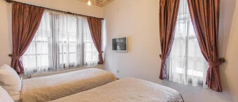 A room with two beds, wooden ceiling, and large windows with curtains.