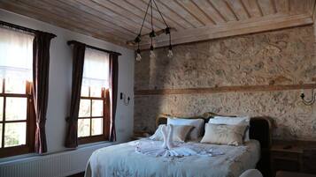 Un dormitorio con pared de piedra, techo de madera y cama con ropa de cama blanca.