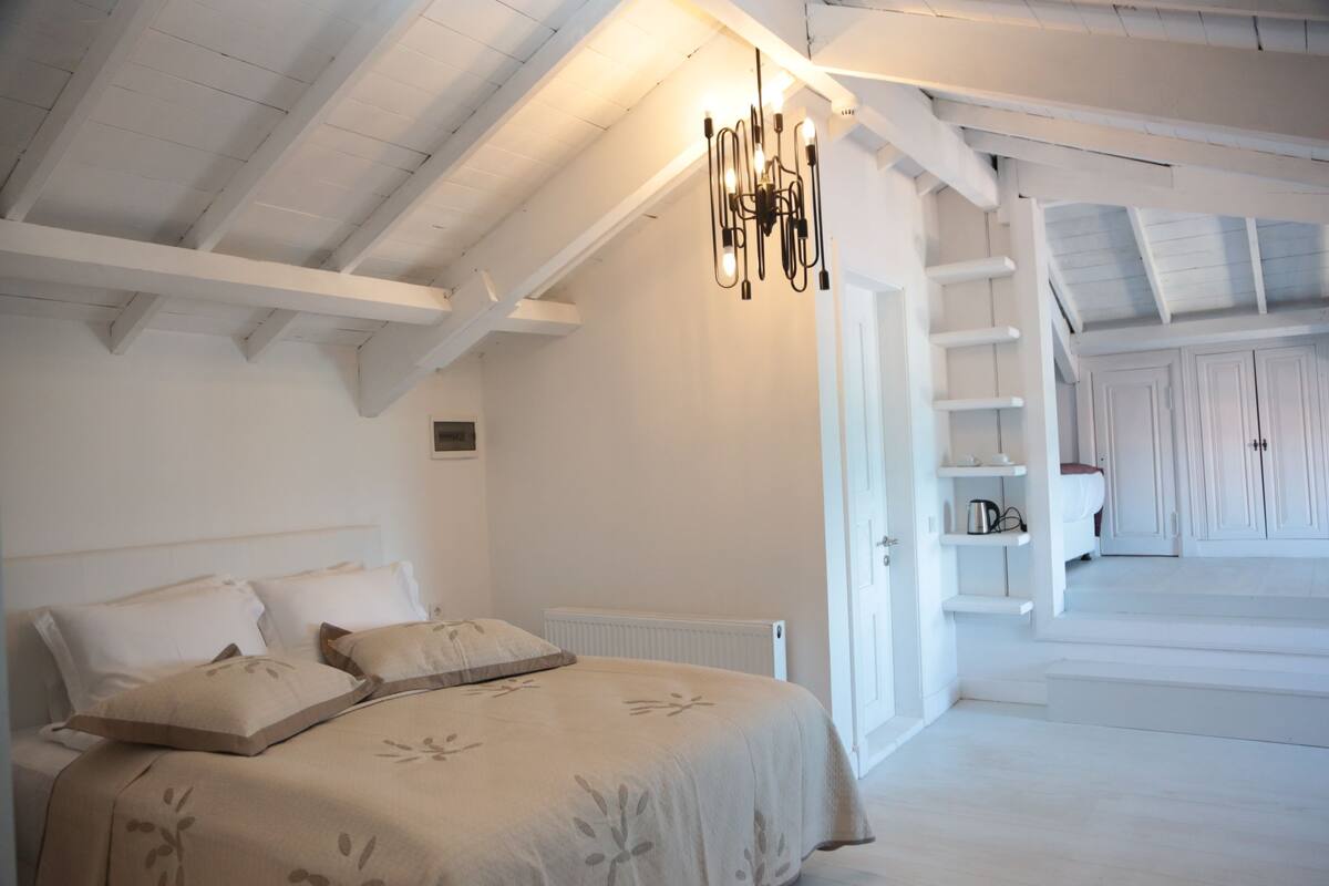 A bedroom with a bed, a radiator, a chandelier, and a staircase leading to a loft area.