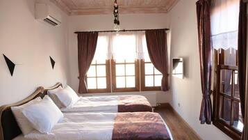 Habitación de hotel con dos camas, techo de madera, unidad de aire acondicionado y ventana con cortinas.