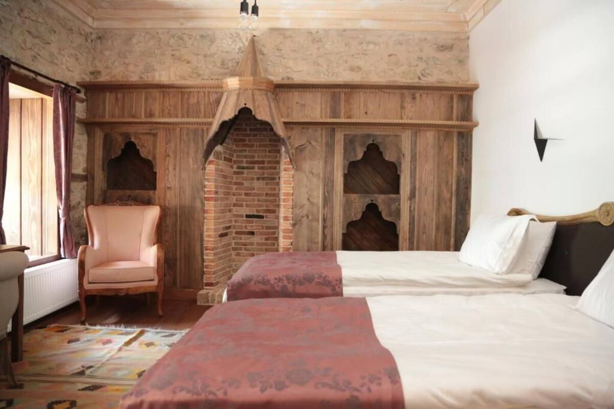 A bedroom with a brick fireplace, a wooden canopy bed, a chair, and a patterned rug.