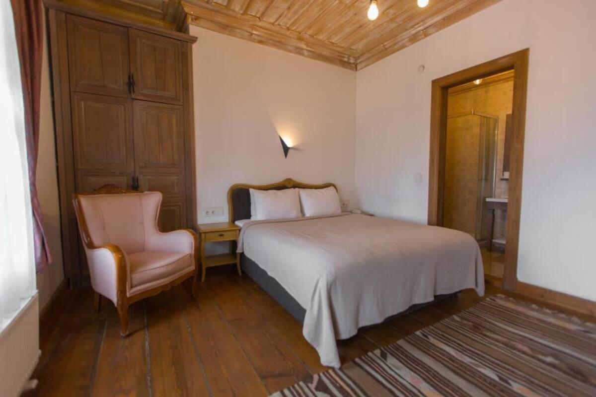 A bedroom with a wooden ceiling, a bed with white bedding, a nightstand, a wooden wardrobe, and a patterned rug.