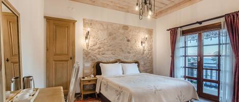 A bedroom with a bed, wooden ceiling, stone wall, and a view through a window with curtains.