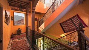 Un intérieur à plusieurs niveaux, agrémenté de balustrades décoratives, offrant une vue sur l’extérieur et orné d’un tapis traditionnel sur l’escalier.