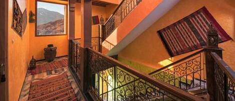 Un interior de varios niveles con barandillas ornamentadas, vistas al exterior y una alfombra tradicional en las escaleras.