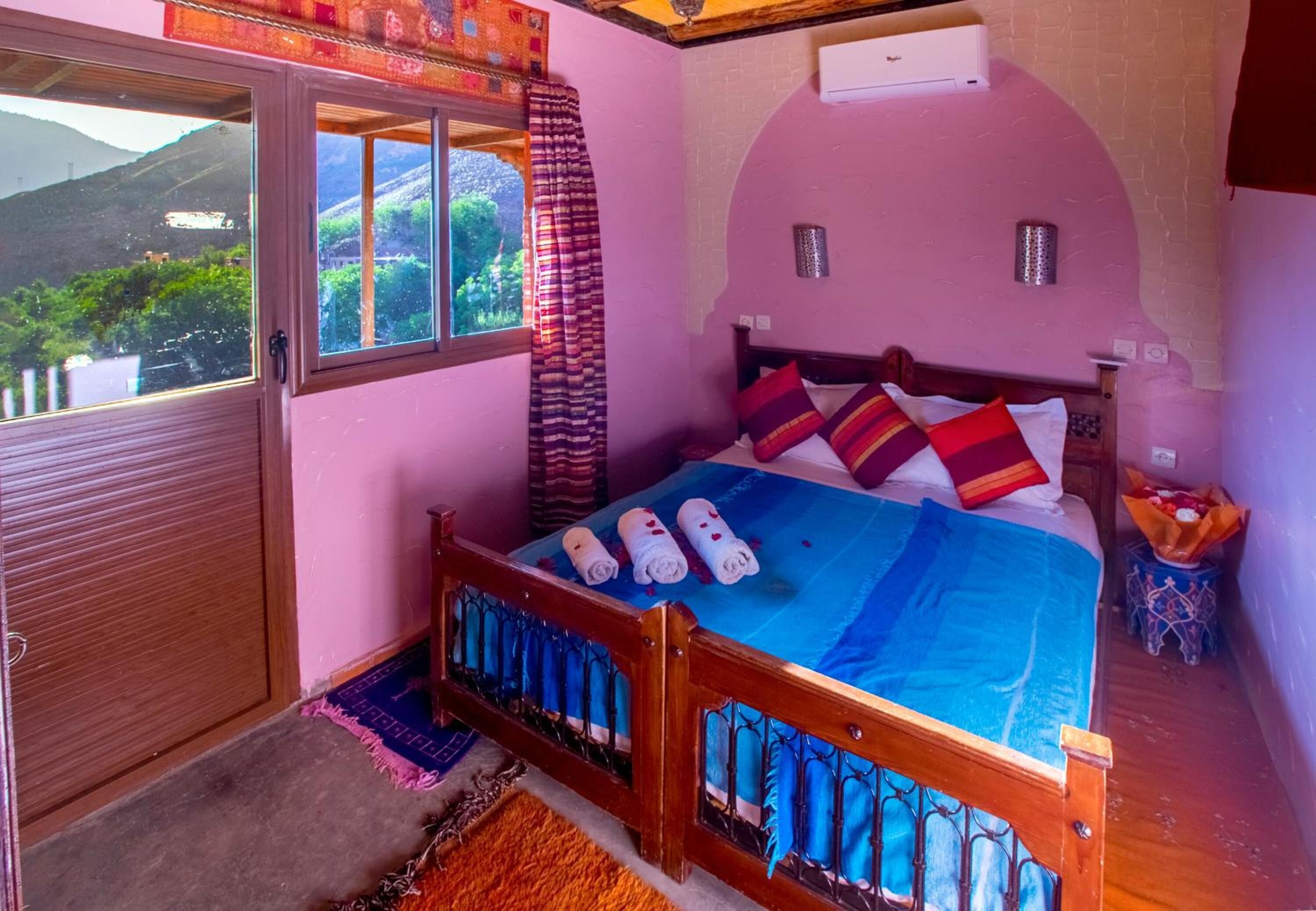 A bedroom with a bed, a window, and a view of greenery.