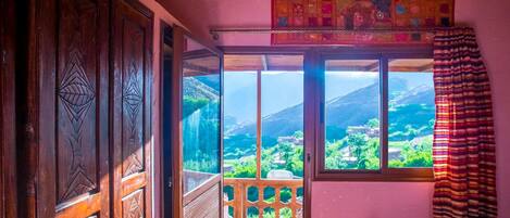 Una habitación con puerta de madera, ventana con vistas a un paisaje montañoso y cortina estampada.