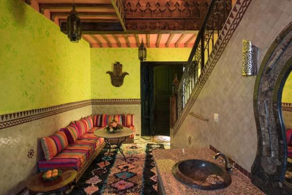 A room with a green wall, a striped sofa, a patterned rug, a round table, and a large mirror.