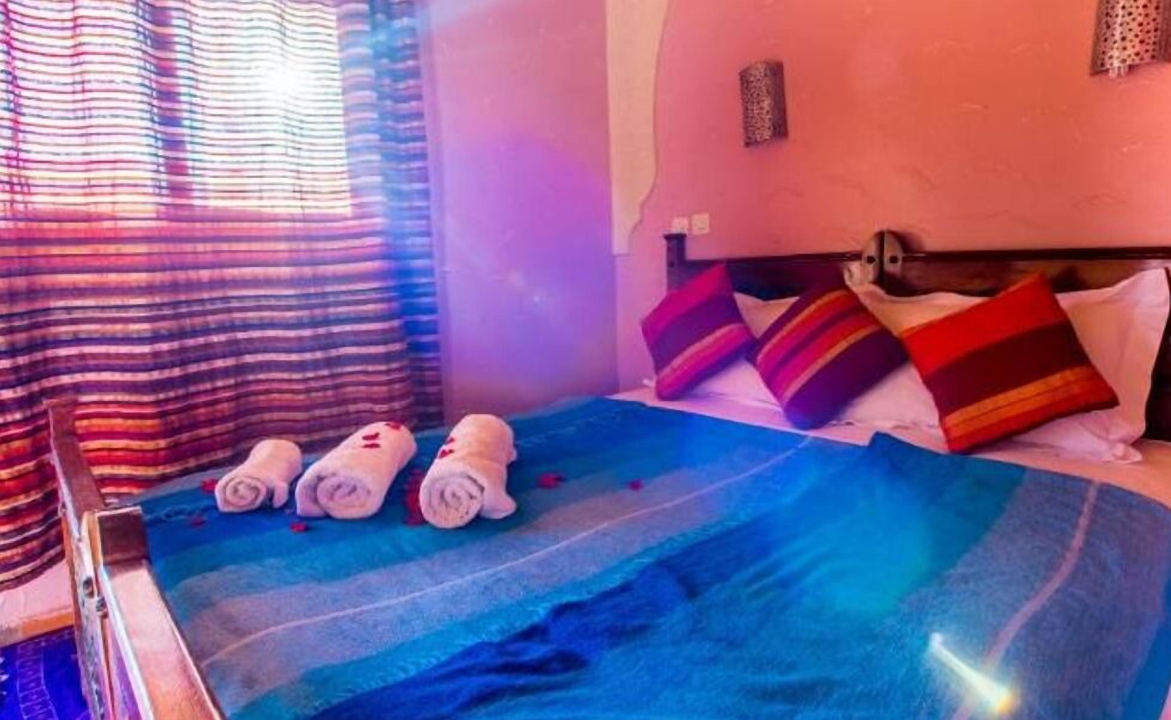 A hotel room with a bed, pillows, and rolled towels.