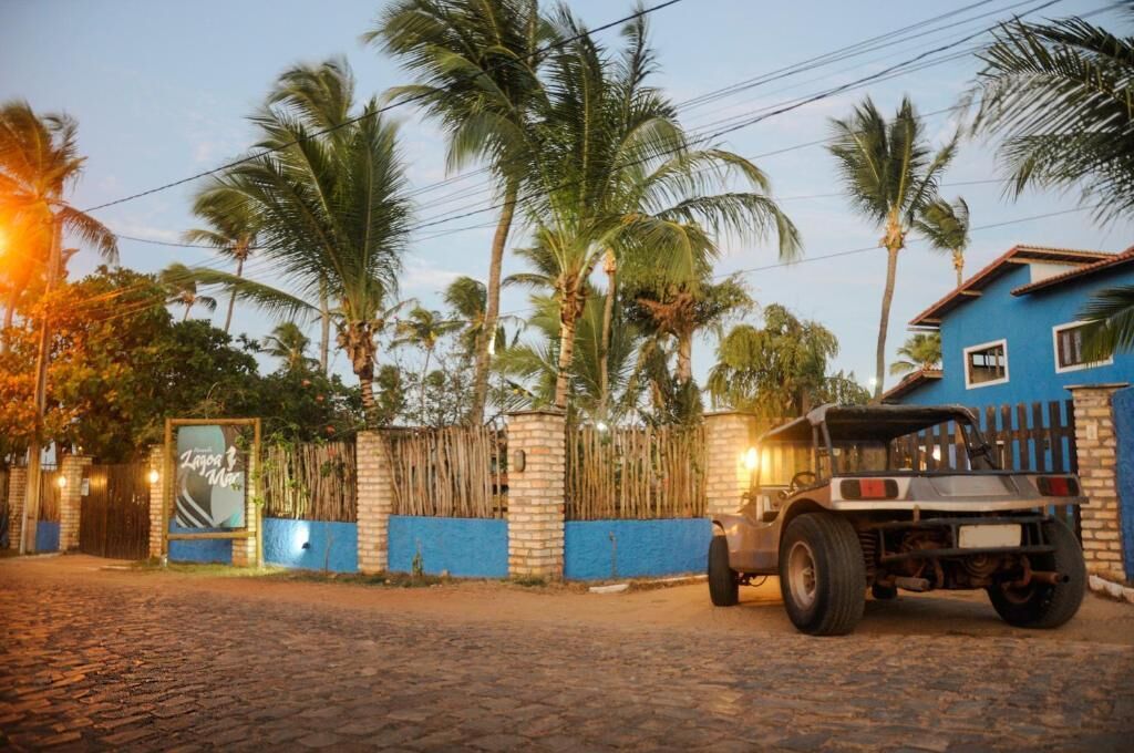 A rustic building with a blue exterior, a vehicle parked in front, and palm trees in the background.