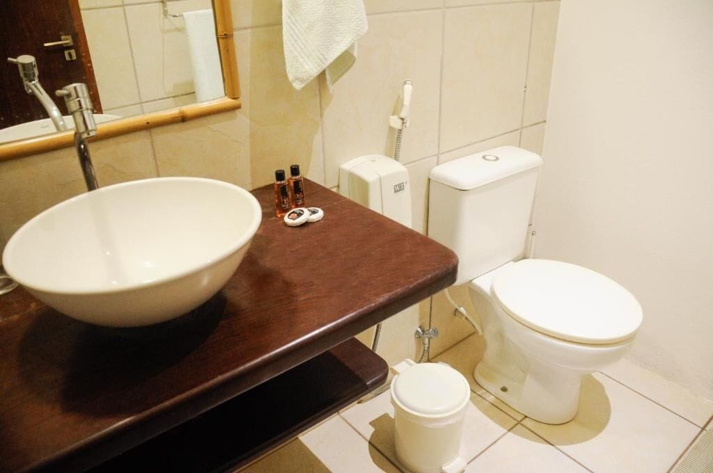 A bathroom with a white sink, a mirror, a towel hanging on the wall, a toilet, and a soap dispenser.