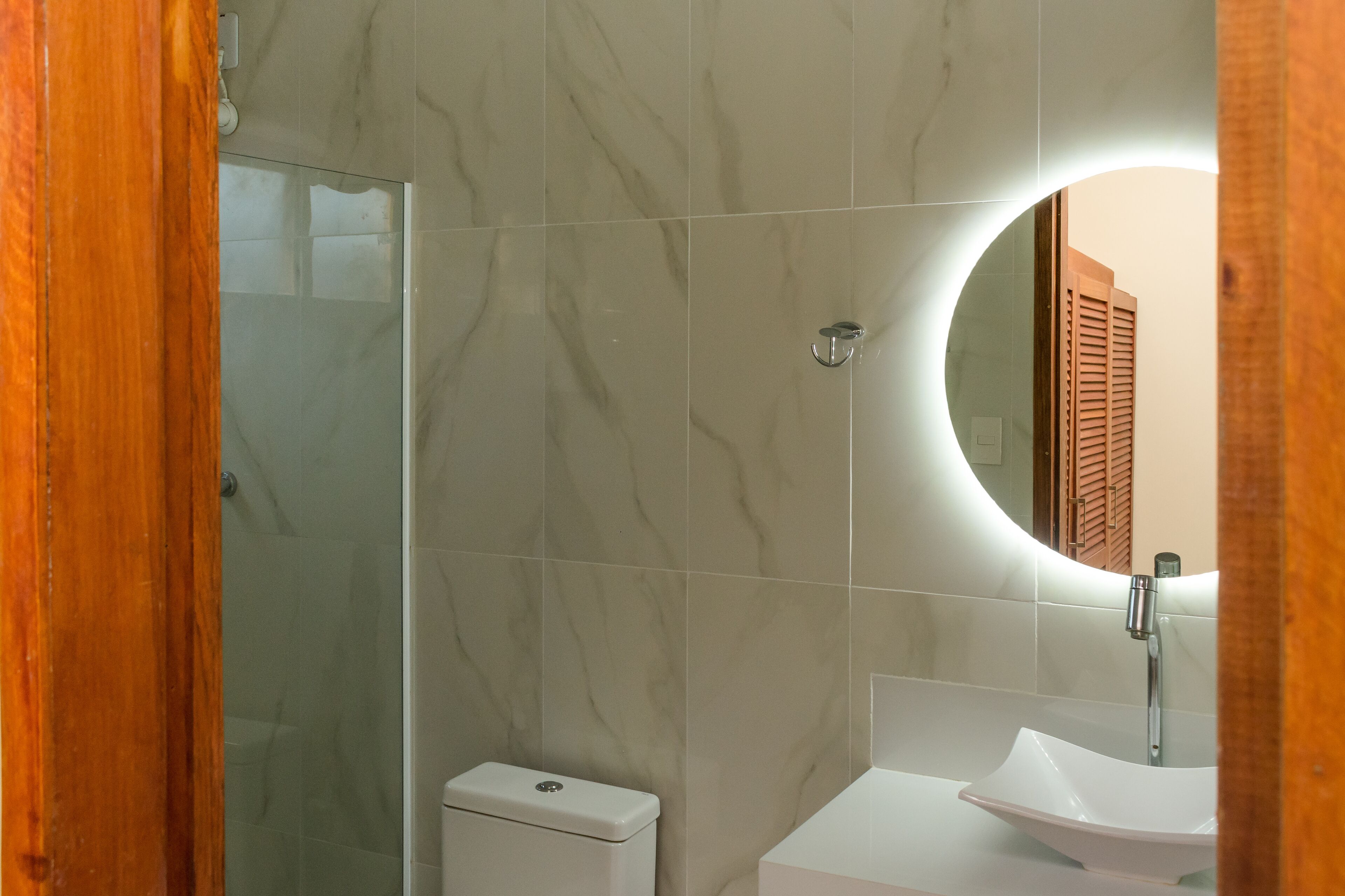 Ein Badezimmer mit Duschkabine aus Glas, Toilette in Weiß, Waschbecken mit weißem Becken und rundem Spiegel.