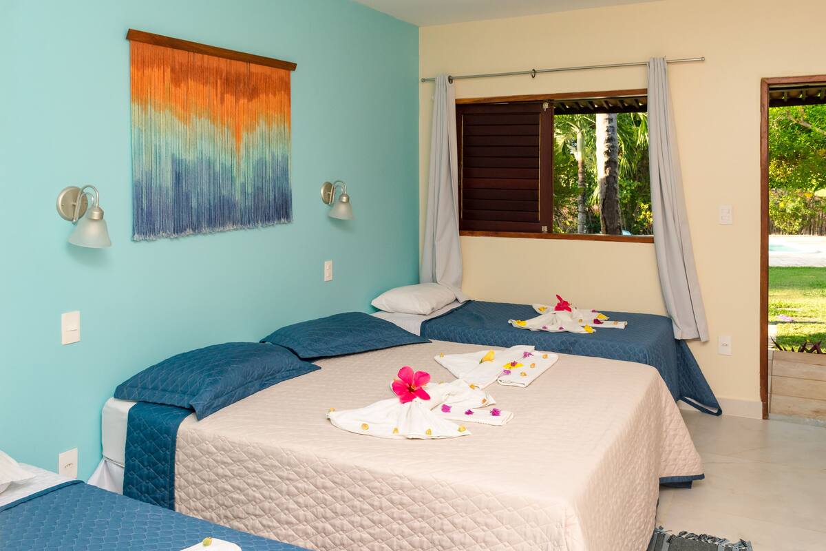 Une chambre d’hôtel avec deux lits, une grande fenêtre avec des rideaux, une lampe fixée au mur et une tapisserie aux couleurs vives.
