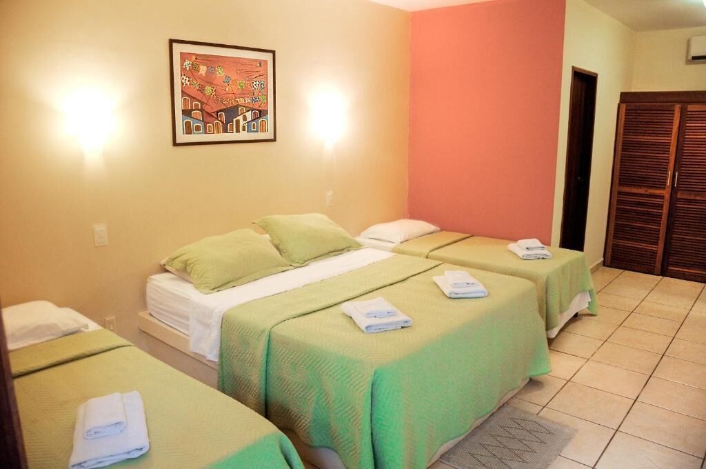Een hotelkamer met twee éénpersoonsbedden, elk met een groene plaid en witte kussens, en een ingelijst beeld aan de muur.
