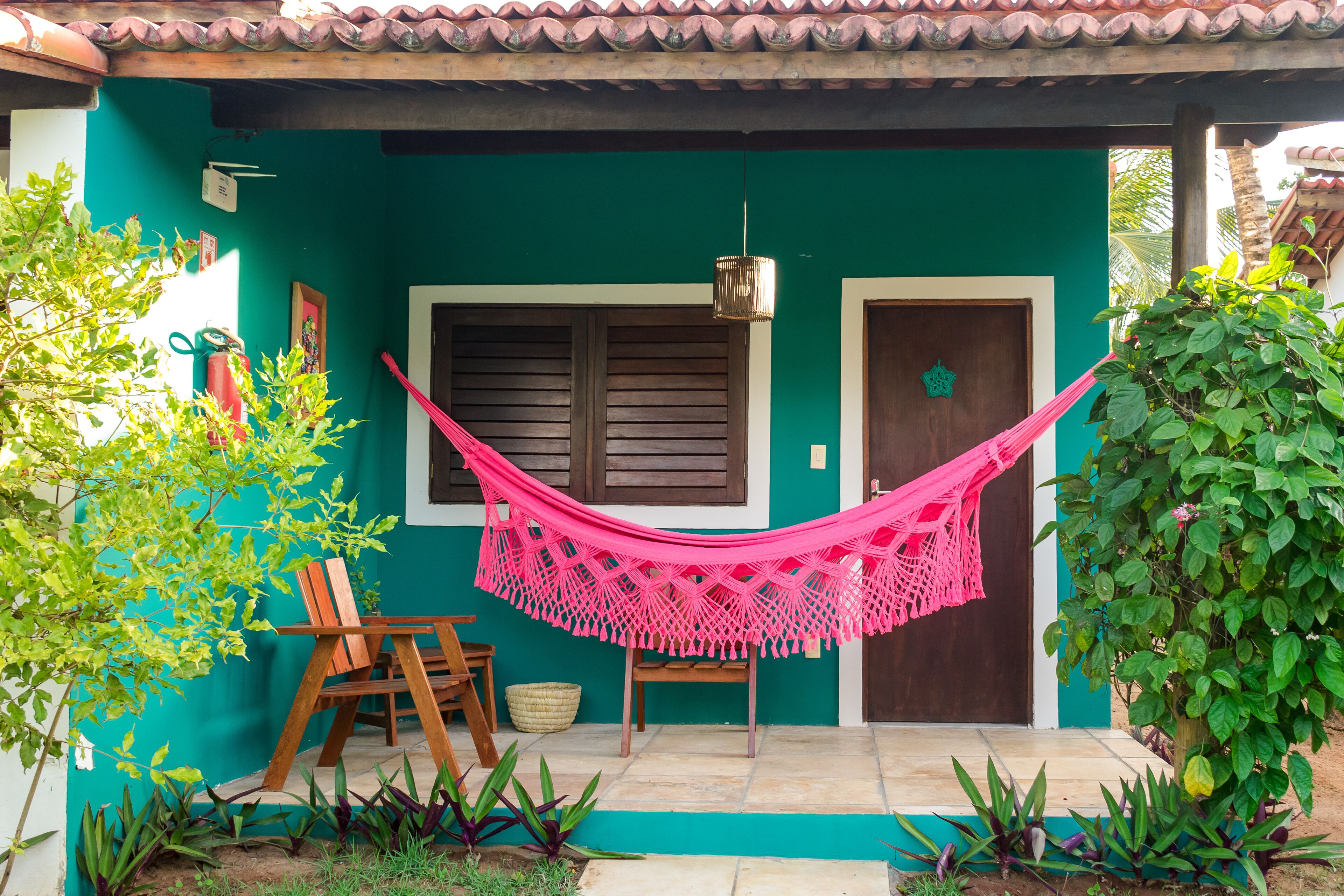 Una casa con fachada verde, una puerta de madera y una hamaca colgada en el porche delantero.