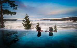 A glass-bottomed infinity pool with a view of a frozen lake and trees. - Orbaden Spa & Resort (Vallsta)