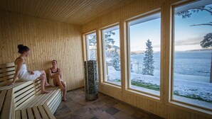 Un sauna en bois, doté de bancs et de grandes fenêtres, qui offre une vue sur un paysage enneigé et sur l’eau.