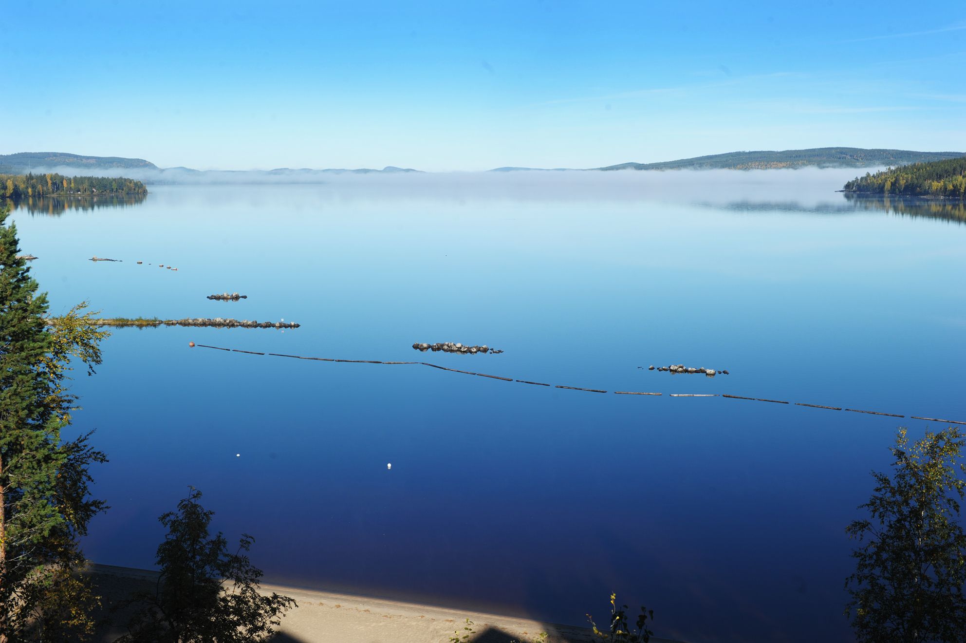 Un lago tranquilo con cielos despejados, rodeado de colinas boscosas.