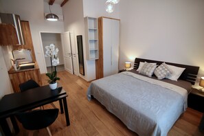 Ein Schlafzimmer mit einem Bett, Nachttischen, einem Schreibtisch und einem Sessel. Es gibt einen Kleiderschrank und einen Spiegel.