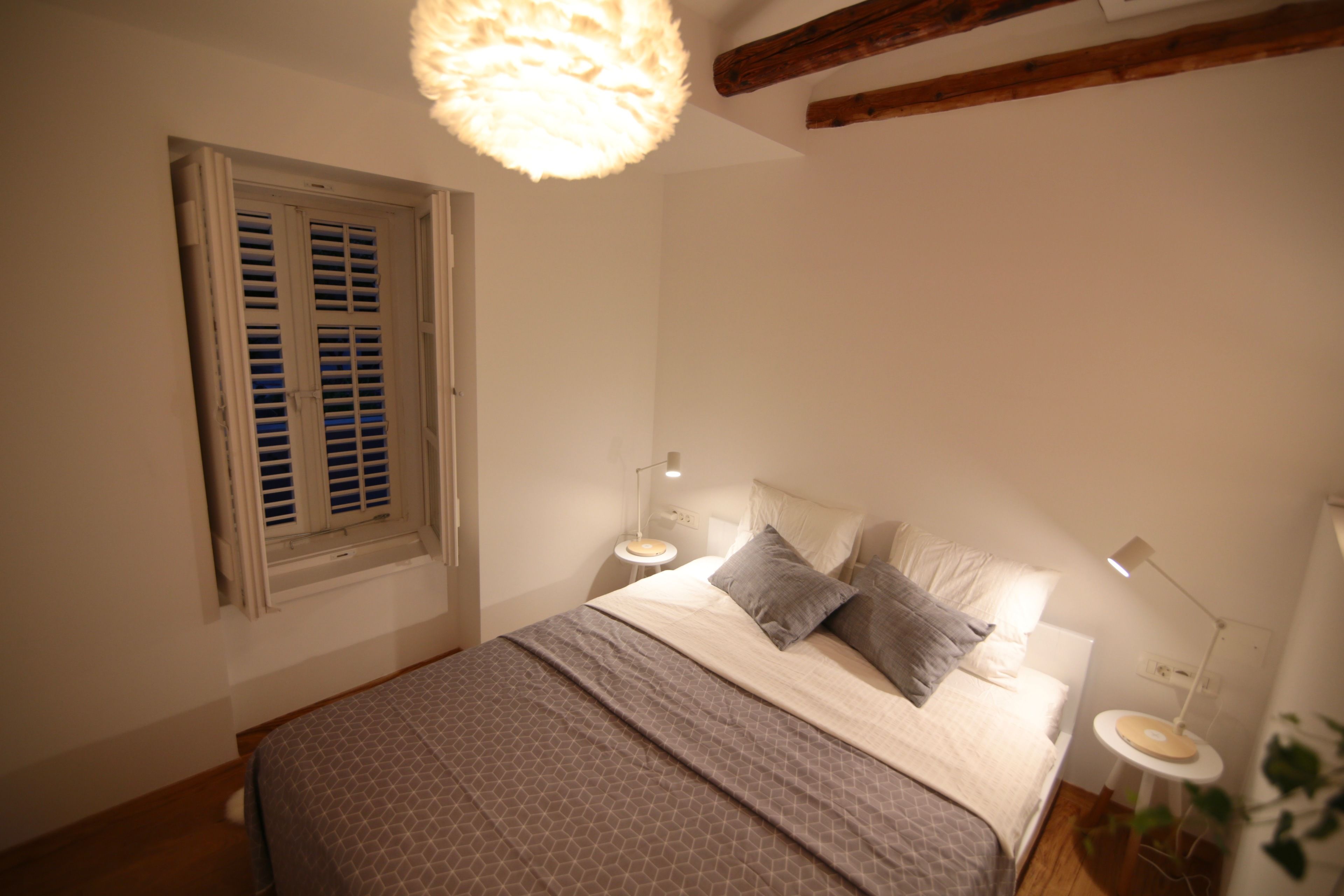 Une chambre à coucher avec un lit, des lampes de chevet, une fenêtre avec des volets et un luminaire au plafond.
