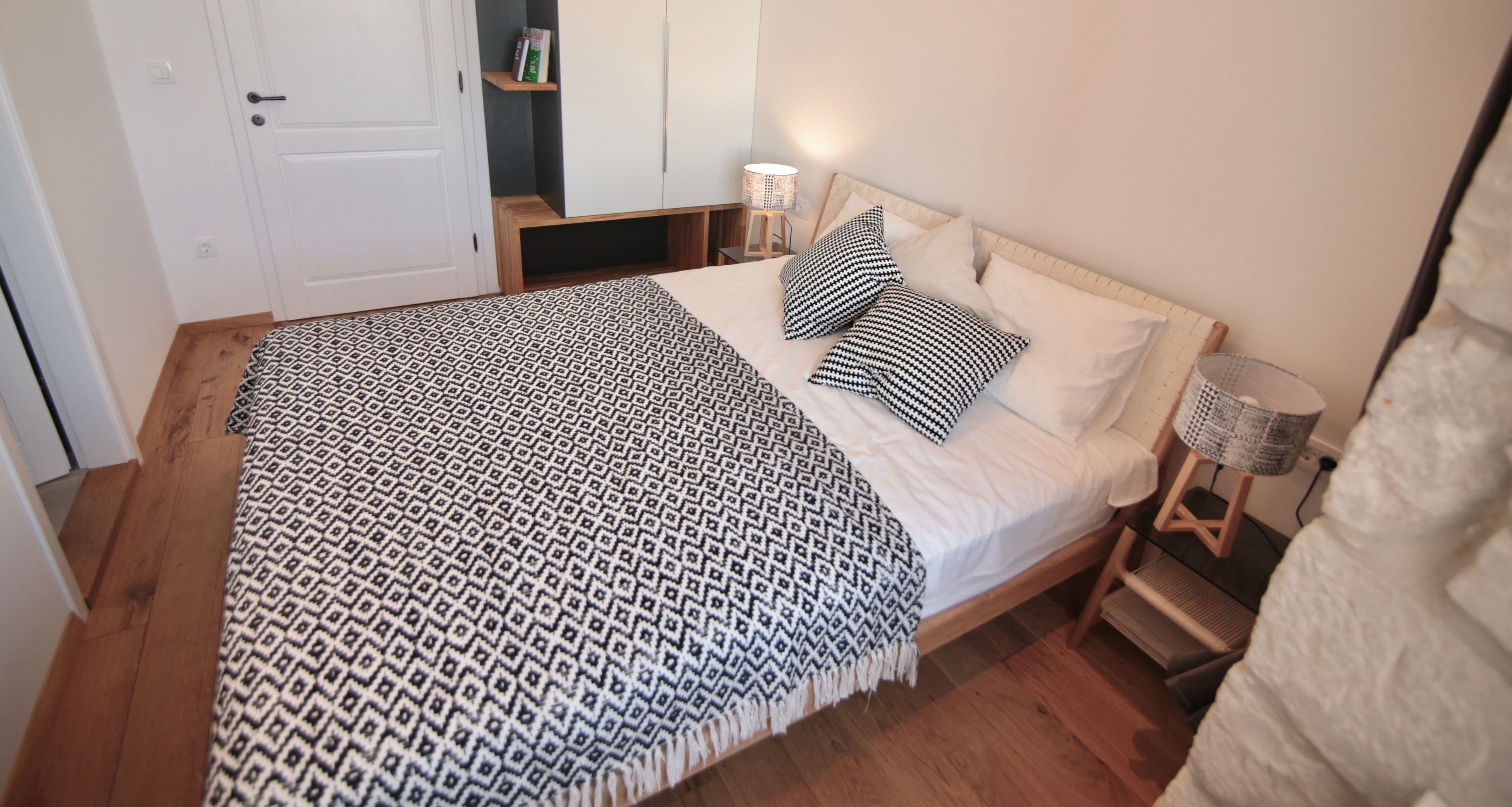 Una cama bien hecha con ropa de cama estampada, una lámpara de noche y una mesita de madera.