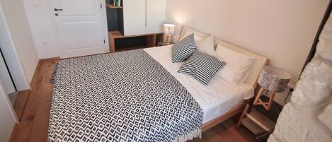 Una cama bien hecha con ropa de cama estampada, una lámpara de noche y una mesita de madera.