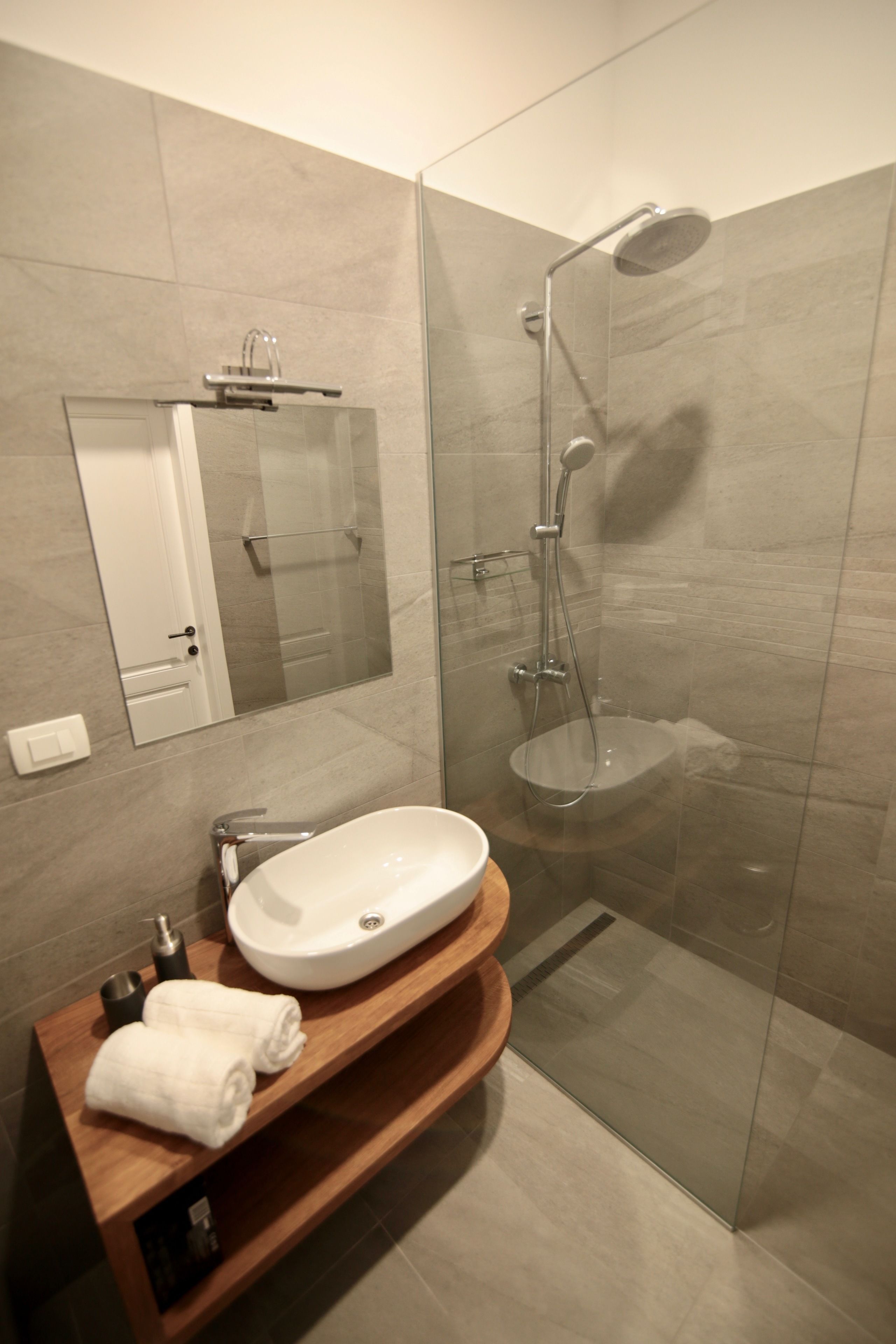 A modern bathroom with a glass-enclosed shower, a white sink, and a wooden vanity.