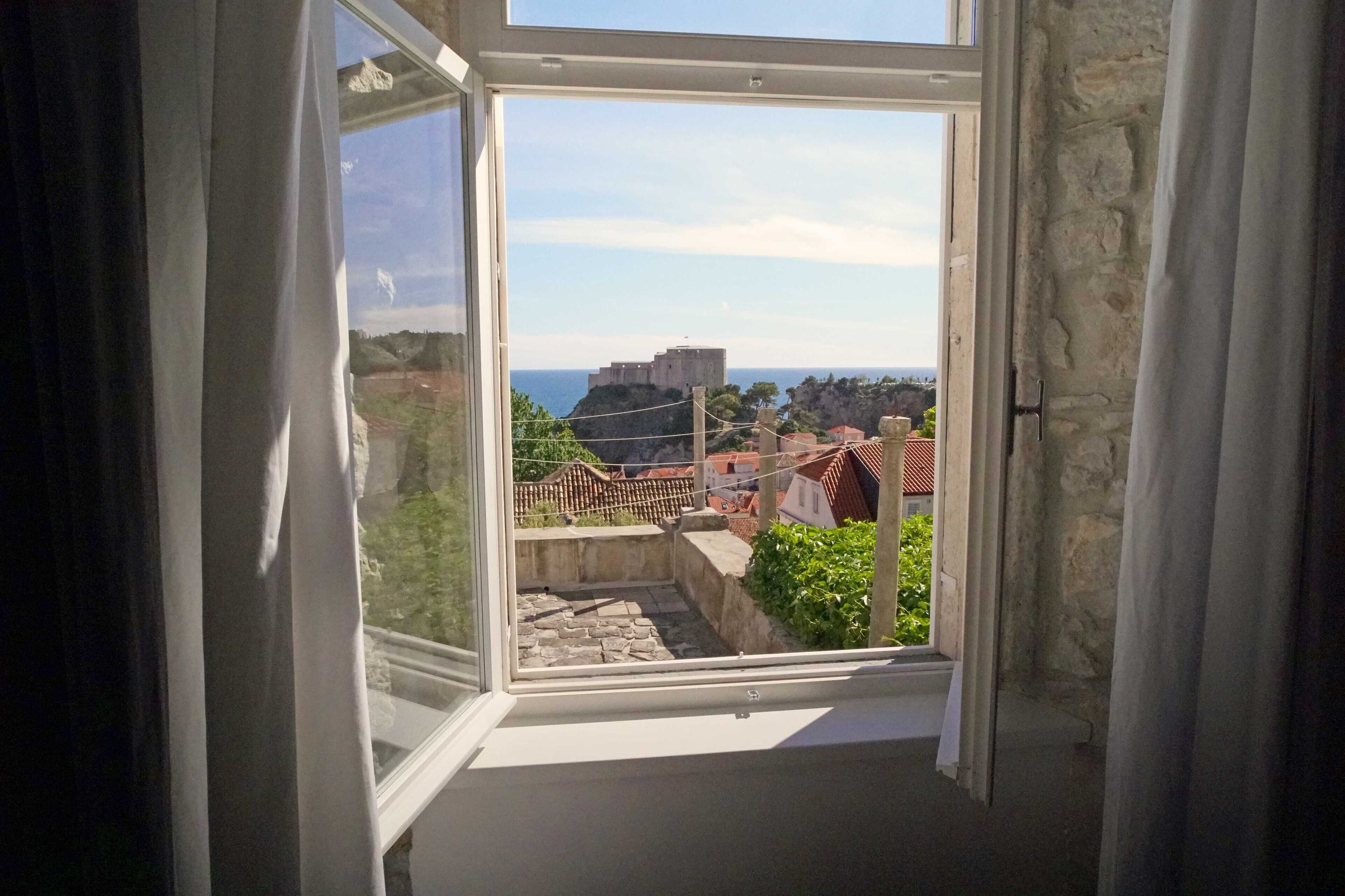 A room with a view of a historic building and a coastal landscape through an open window.
