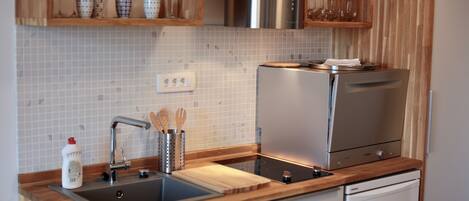 A modern kitchen with a stainless steel refrigerator, a built-in oven, a sink with a wooden countertop, and a backsplash of white tiles.