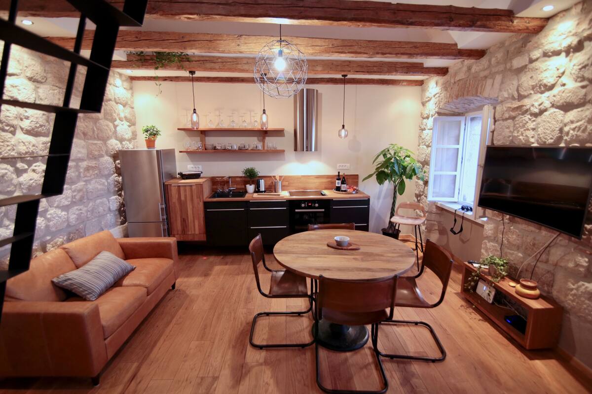 Een moderne keuken met een houten eettafel, een bank en een aan de muur bevestigde televisie.