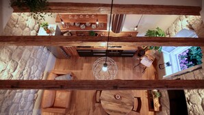 Un interior moderno con pared de piedra, muebles de madera, zona de comedor con lámparas colgantes y televisor montado en la pared.