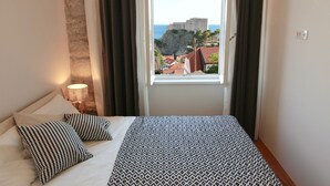Un dormitorio con cama, ventana con cortinas, lámpara de pared y vista a un edificio.
