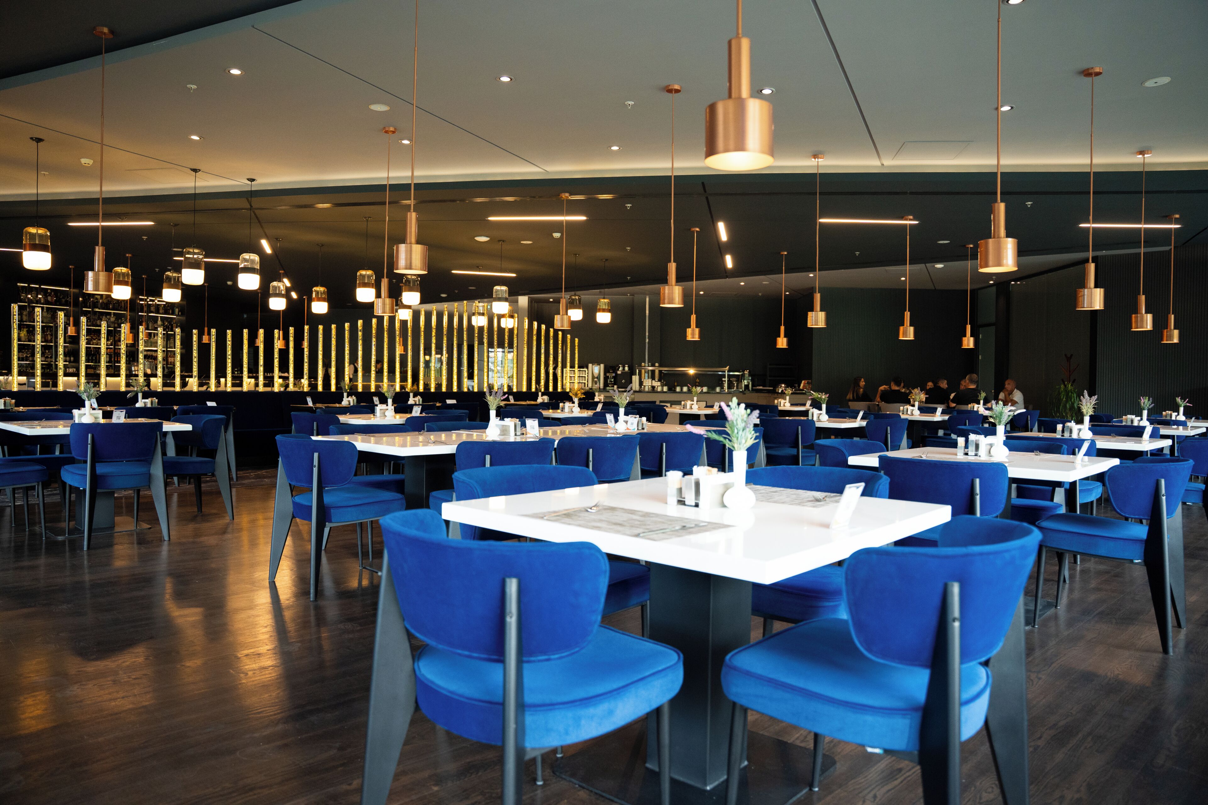 Un'ampia sala da pranzo con diversi tavoli e sedie, illuminazione a sospensione moderna e un'area bar sullo sfondo.