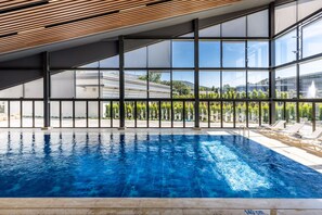 A swimming pool with clear blue water, surrounded by large windows offering views of greenery and buildings. - The Fortyfive Business Hotel & Spa (Manisa)