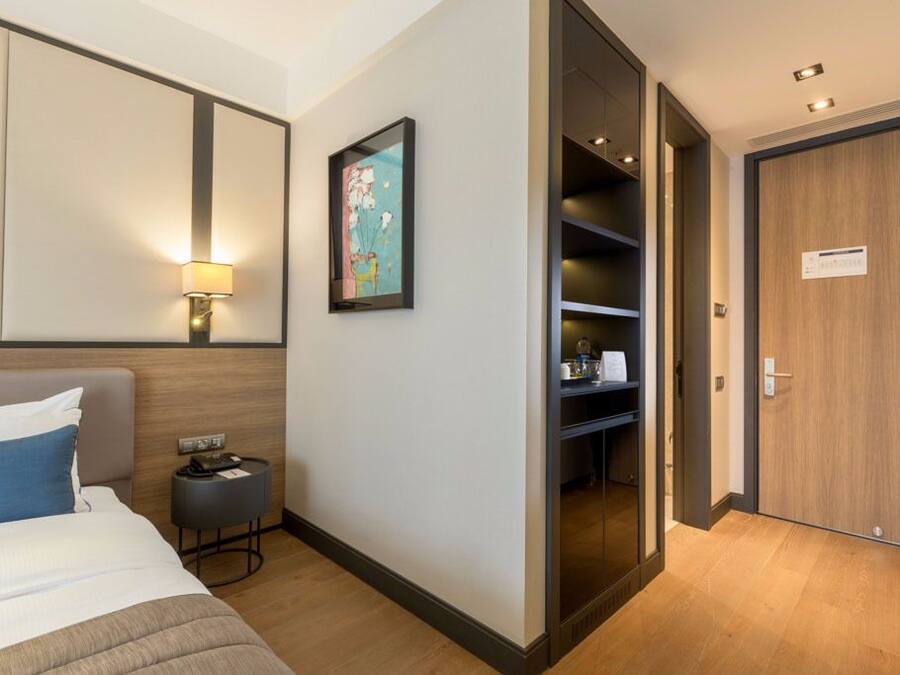 Een hotelkamer met een bed, nachtkastje, lamp, kunstwerk, kledingkast en een inloopkast.