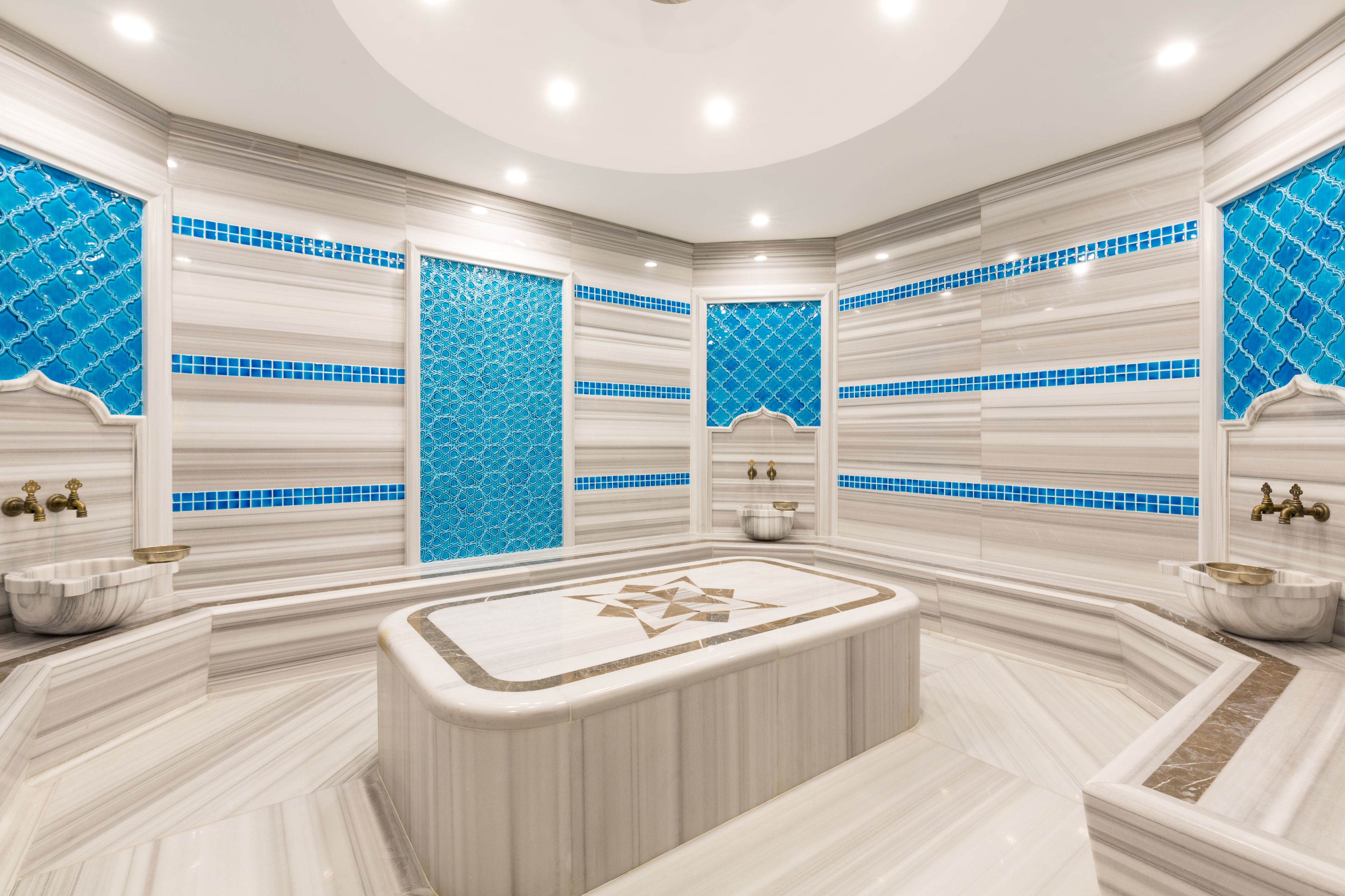 Un baño lujoso con una amplia bañera de mármol, azulejos de mosaico azul y detalles dorados.