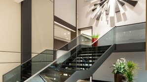 Un intérieur moderne avec un escalier en verre, une œuvre d’art contemporaine murale et des plantes en pot.