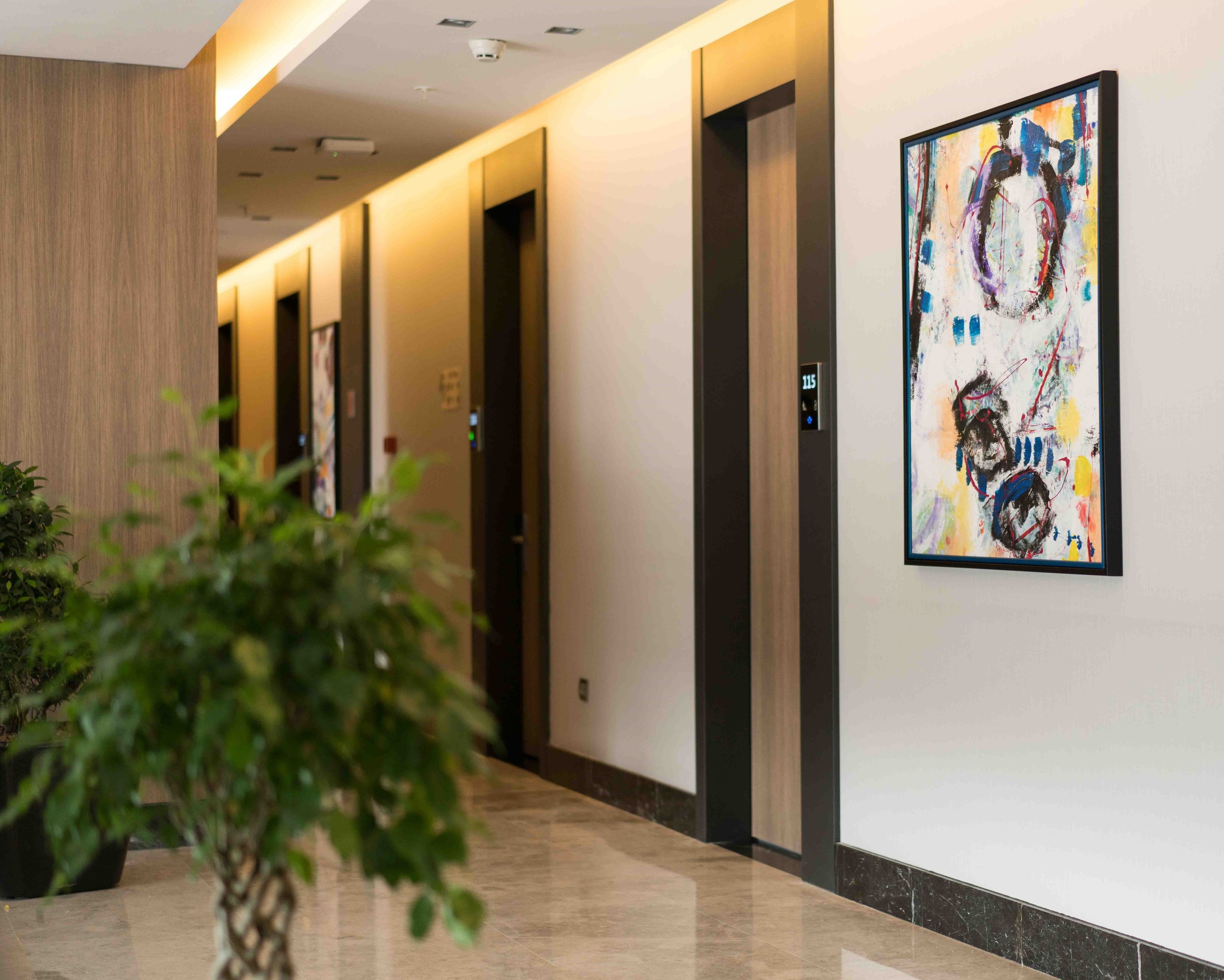 A modern hotel corridor with a marble floor, wooden paneling, and a colorful abstract painting on the wall.