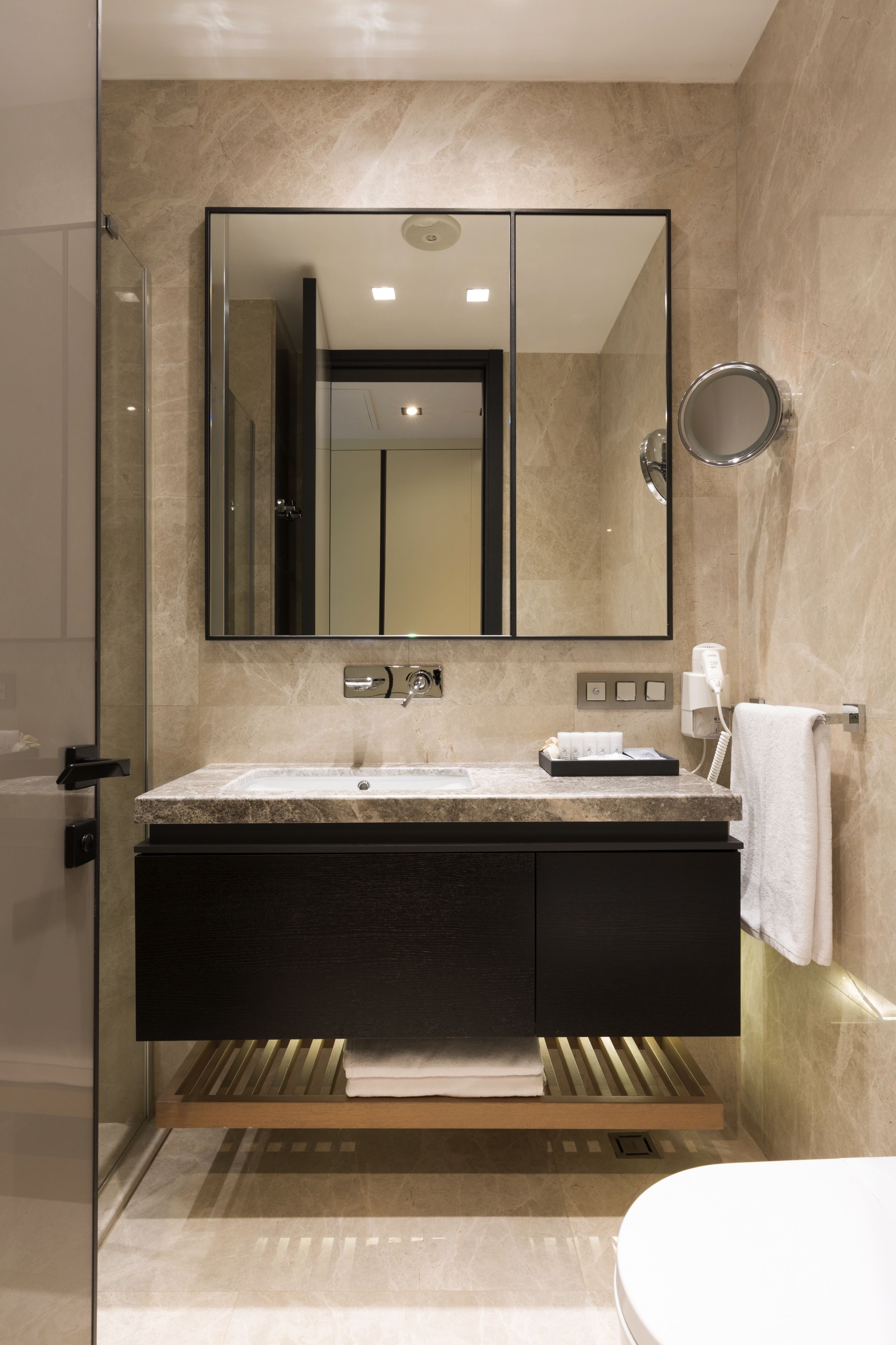 A modern bathroom with a glass shower enclosure, a marble sink, and a large mirror above the vanity.