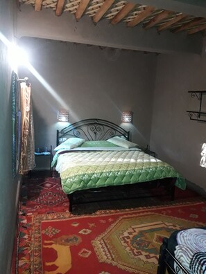 Une chambre à coucher avec un lit, une table de chevet, une lampe fixée au mur et un tapis à motifs.