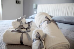 A neatly made bed with rolled white towels tied with gray ribbons. - Soho B&B (Fisciano)