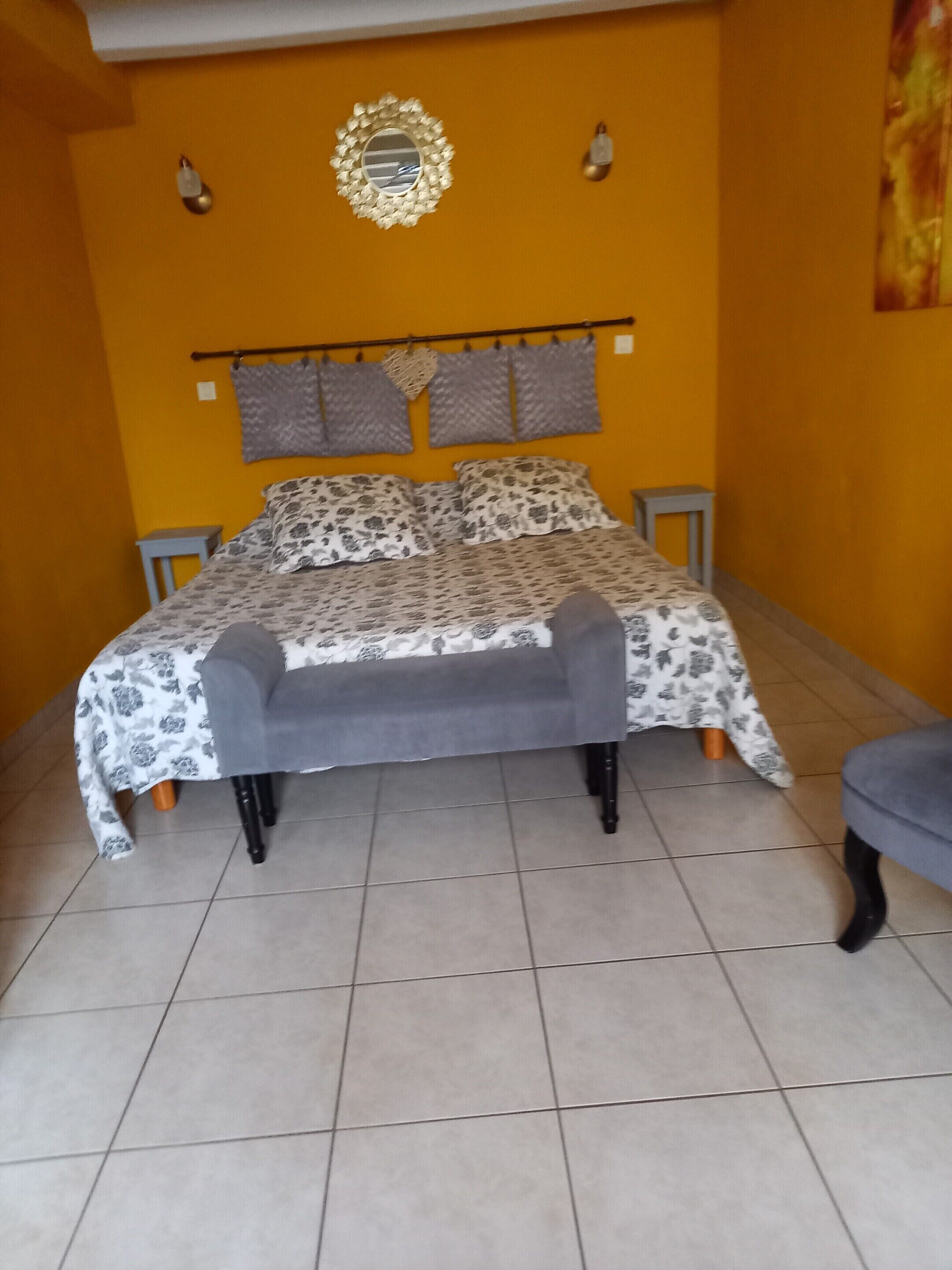 Un dormitorio con cama, mesita de noche, silla y espejo montado en la pared.