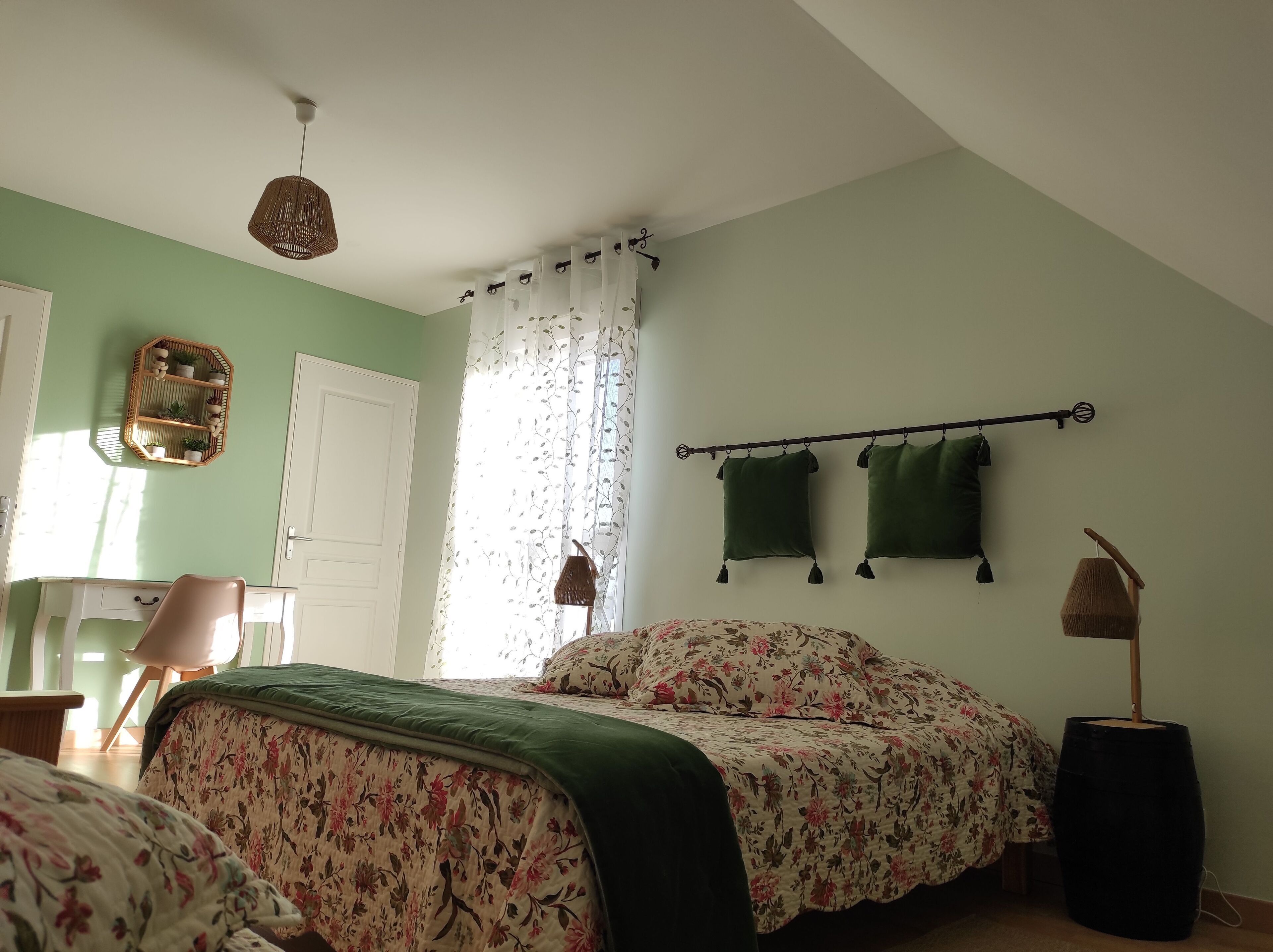 Un dormitorio con cama, una silla, mesita de noche, lámpara colgante y ventana con cortinas.