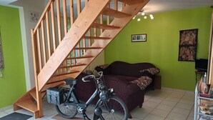 A room with a wooden staircase, a sofa, a bicycle, and a shelf with books. - Le Logis du Livier (Doué-en-Anjou)