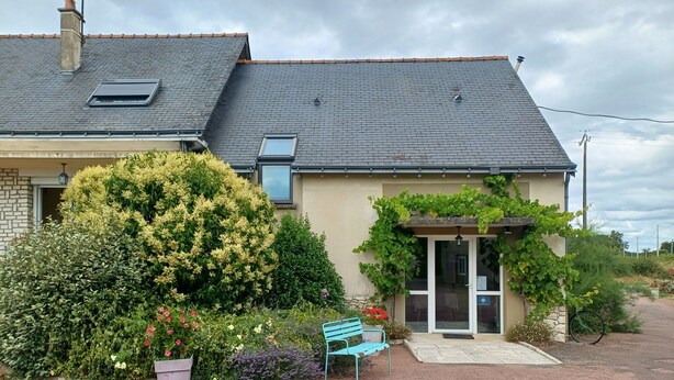 A house with a tiled roof, a garden with various plants and flowers, a bench, and a pathway leading to the entrance. - Le Logis du Livier (Doué-en-Anjou)