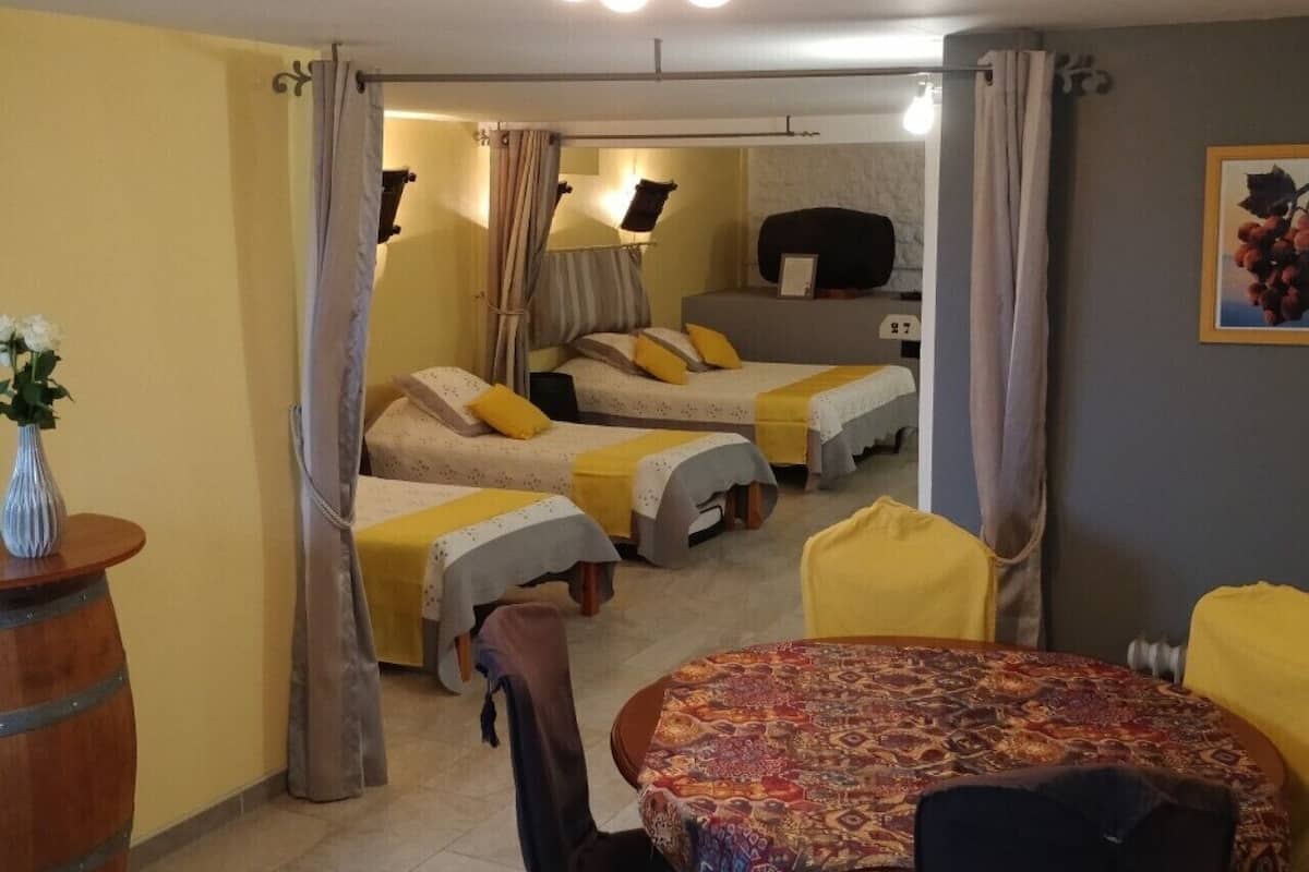 A room with two single beds, a round table with a patterned tablecloth, and a small bar area.