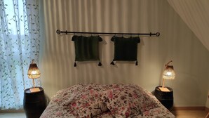 A bedroom with a bed, floral bedding, two hanging towels, and bedside lamps. - Le Logis du Livier (Doué-en-Anjou)