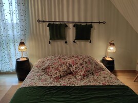 Un dormitorio con una cama, ropa de cama floral, dos toallas colgadas y lámparas de noche.