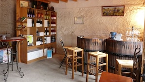 A rustic interior with wooden shelves displaying various bottles, a wooden bar area with stools, and a stone wall. - Le Logis du Livier (Doué-en-Anjou)