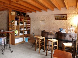 Un interior rústico con estantes de madera que exhiben varias botellas, una zona de bar de madera con taburetes y una pared de piedra.